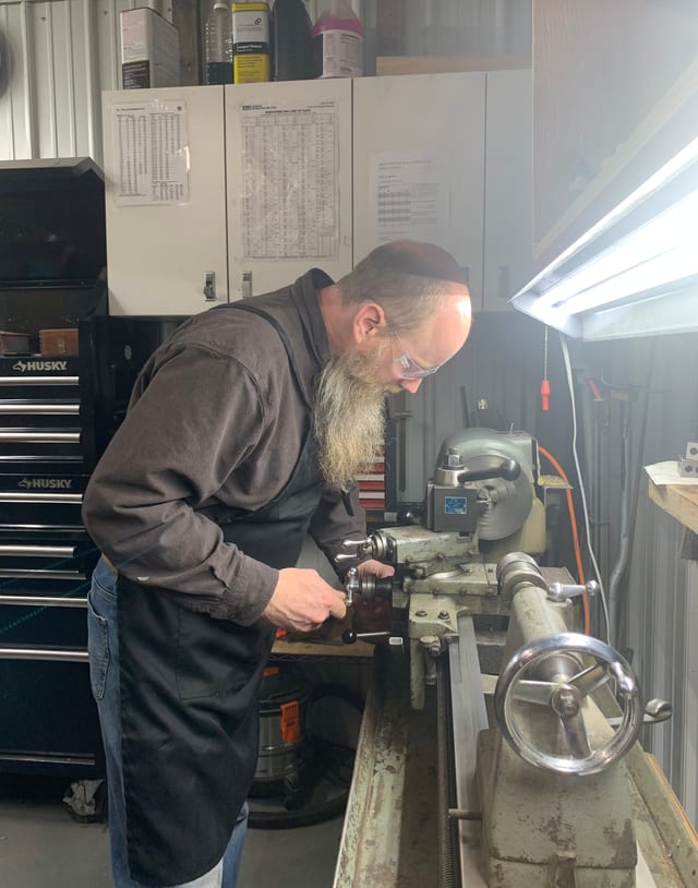 Ben at the milling machine in safety glasses, cutting a firearm part for a custom job.