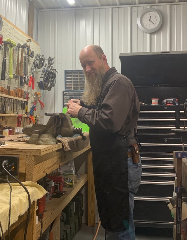 Ben at the workbench with a firearm secured in a vise, working on a repair.